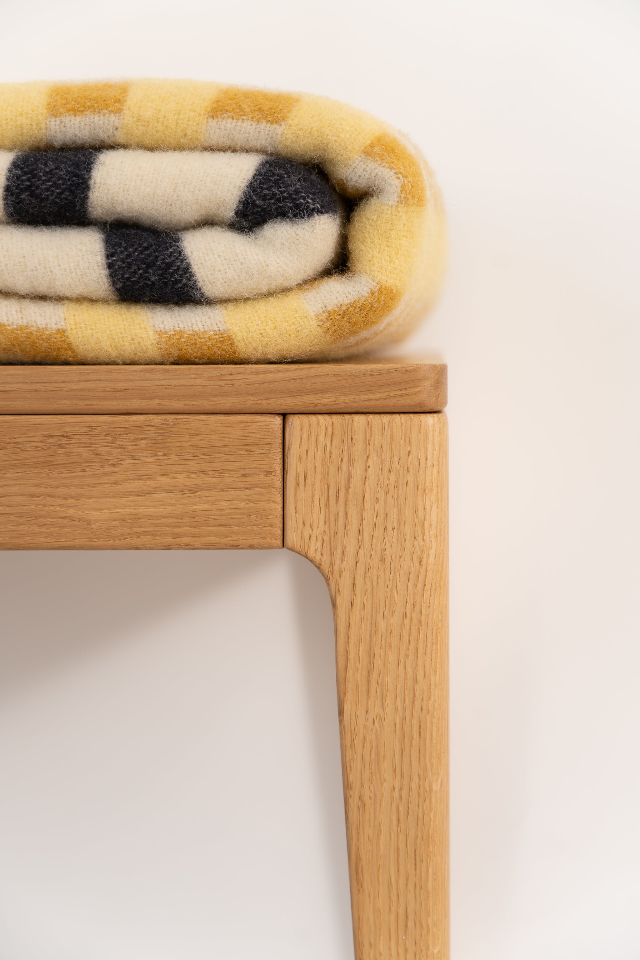 Folded yellow and black plaid blanket on a wooden bench.