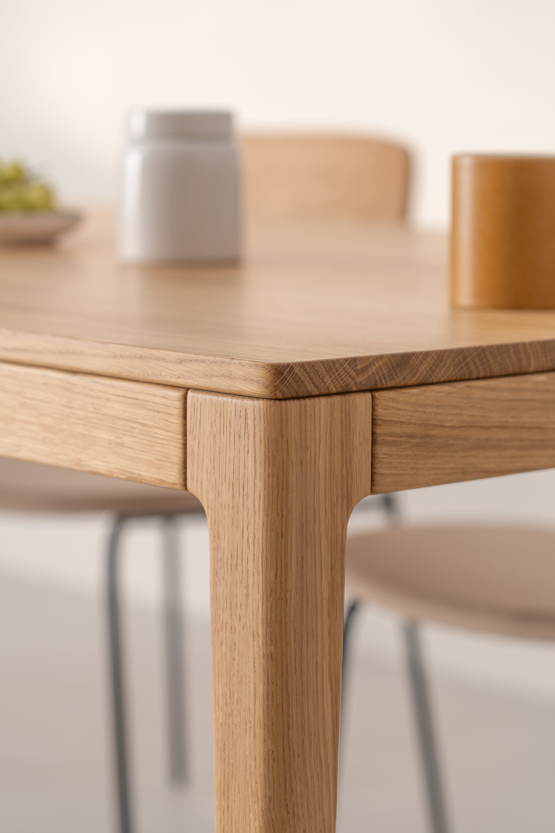 Close-up of the corner of a wooden table with blurry items on top in the background.