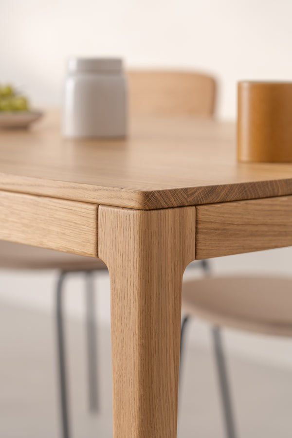 Close-up of the corner of a wooden table with blurry items on top in the background.