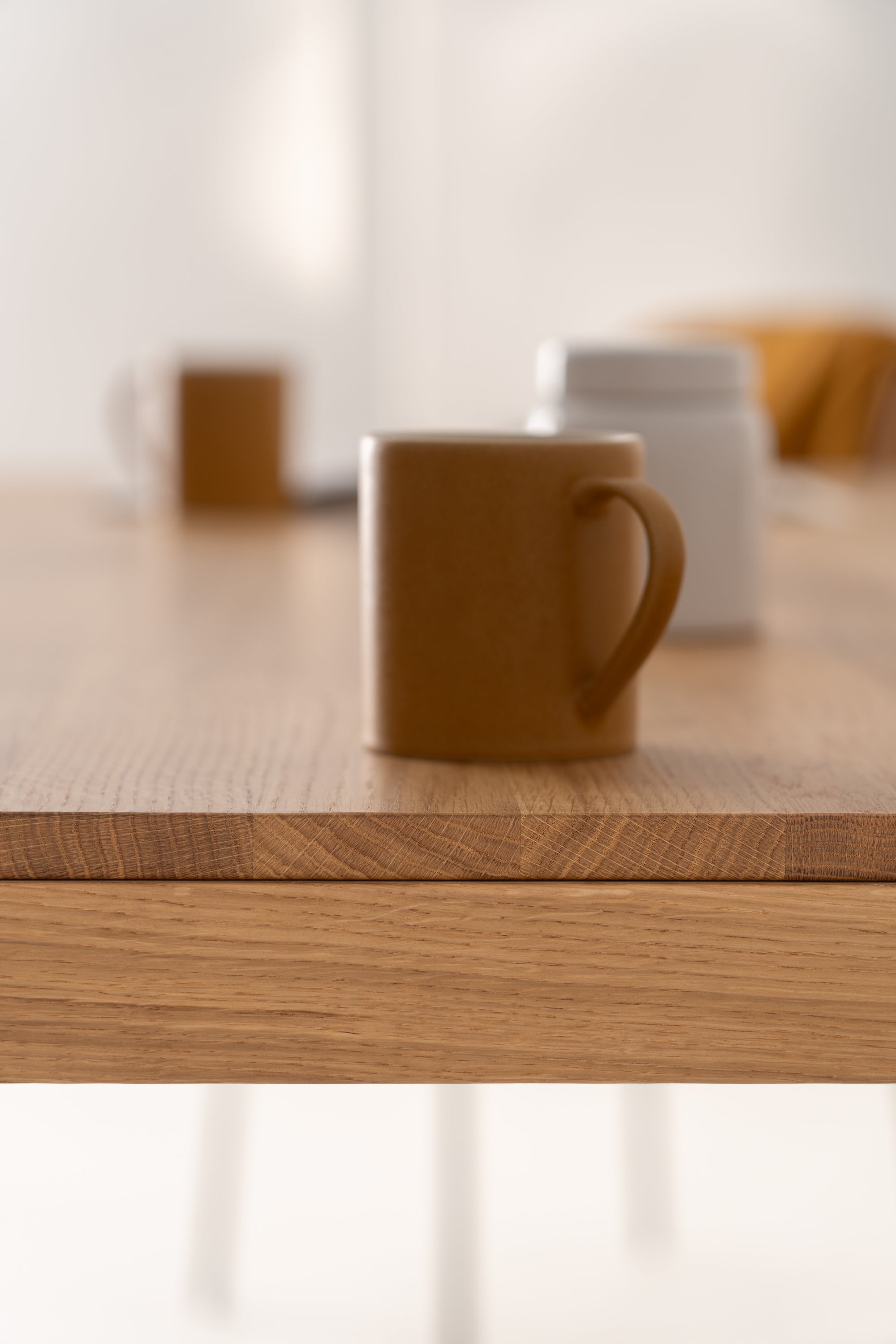 Brown ceramic mug on a wooden table with blurred objects in the background.