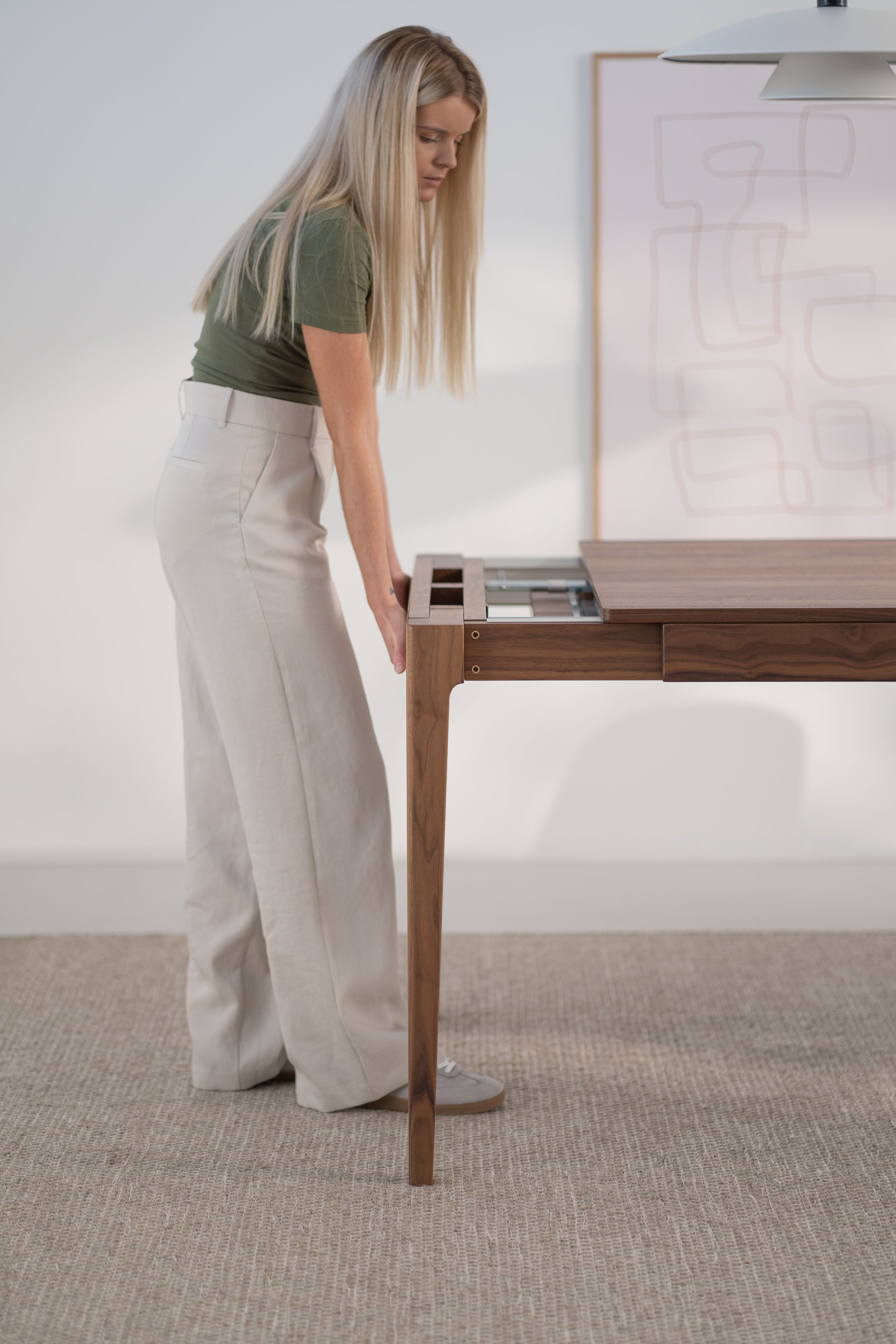 Woman adjusting a wooden table with storage in a minimalist room.