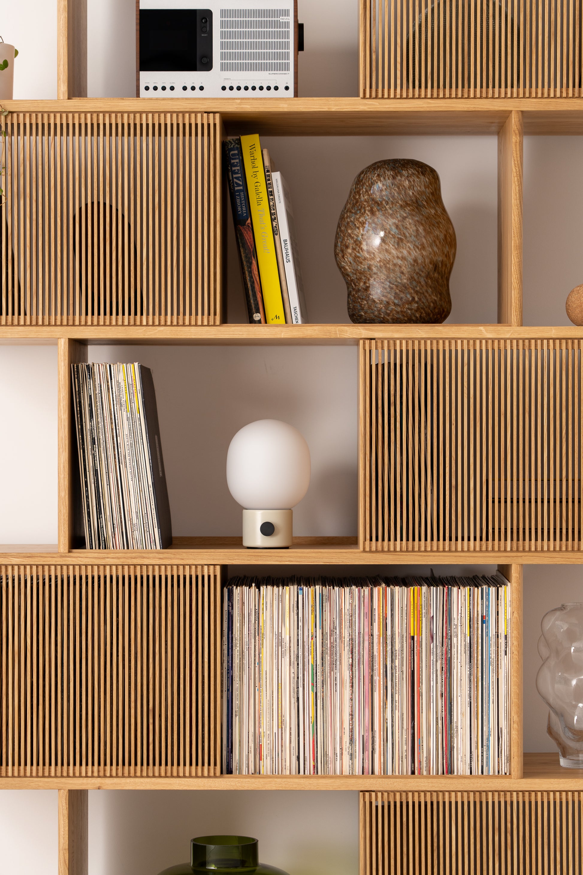 Wooden shelves with books, magazines, a radio, a ceramic vase, and a small lamp.