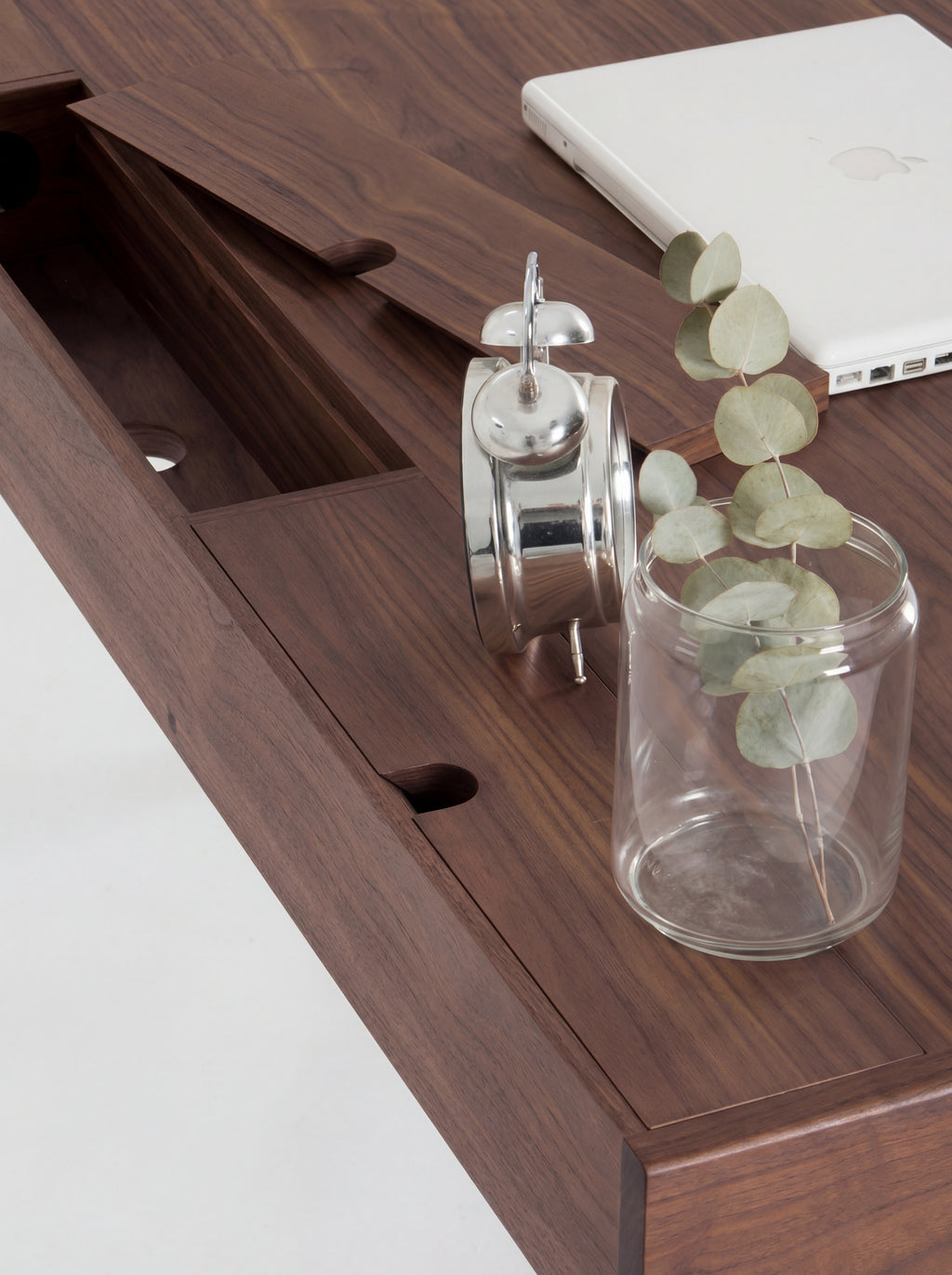 Top-down view of an open cable flap on the HEIM 140 desk in walnut wood, beside a glass vase of eucalyptus