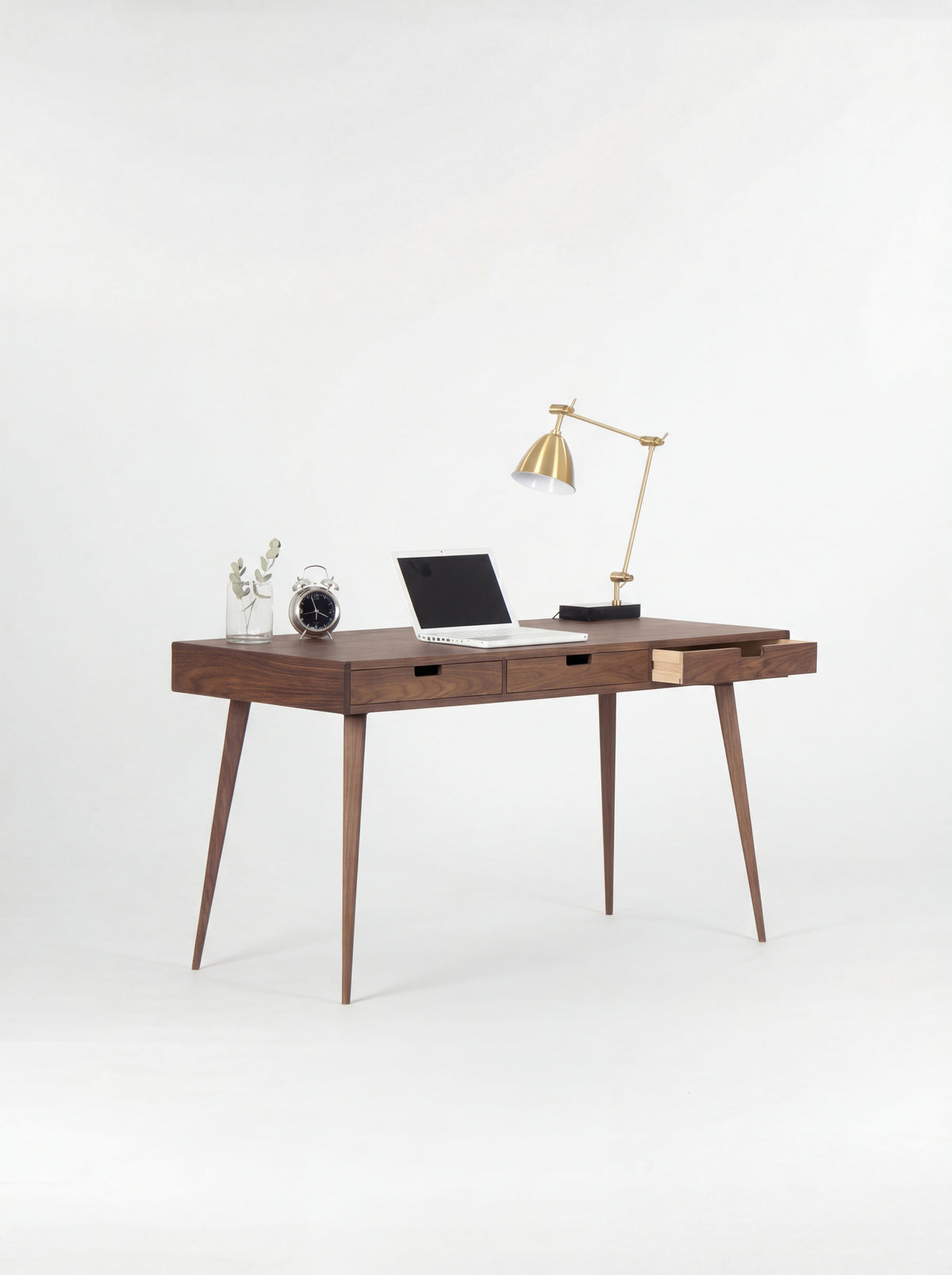 HEIM 140 writing desk in walnut wood, three-quarter view with the right drawer open, a laptop and brass lamp
