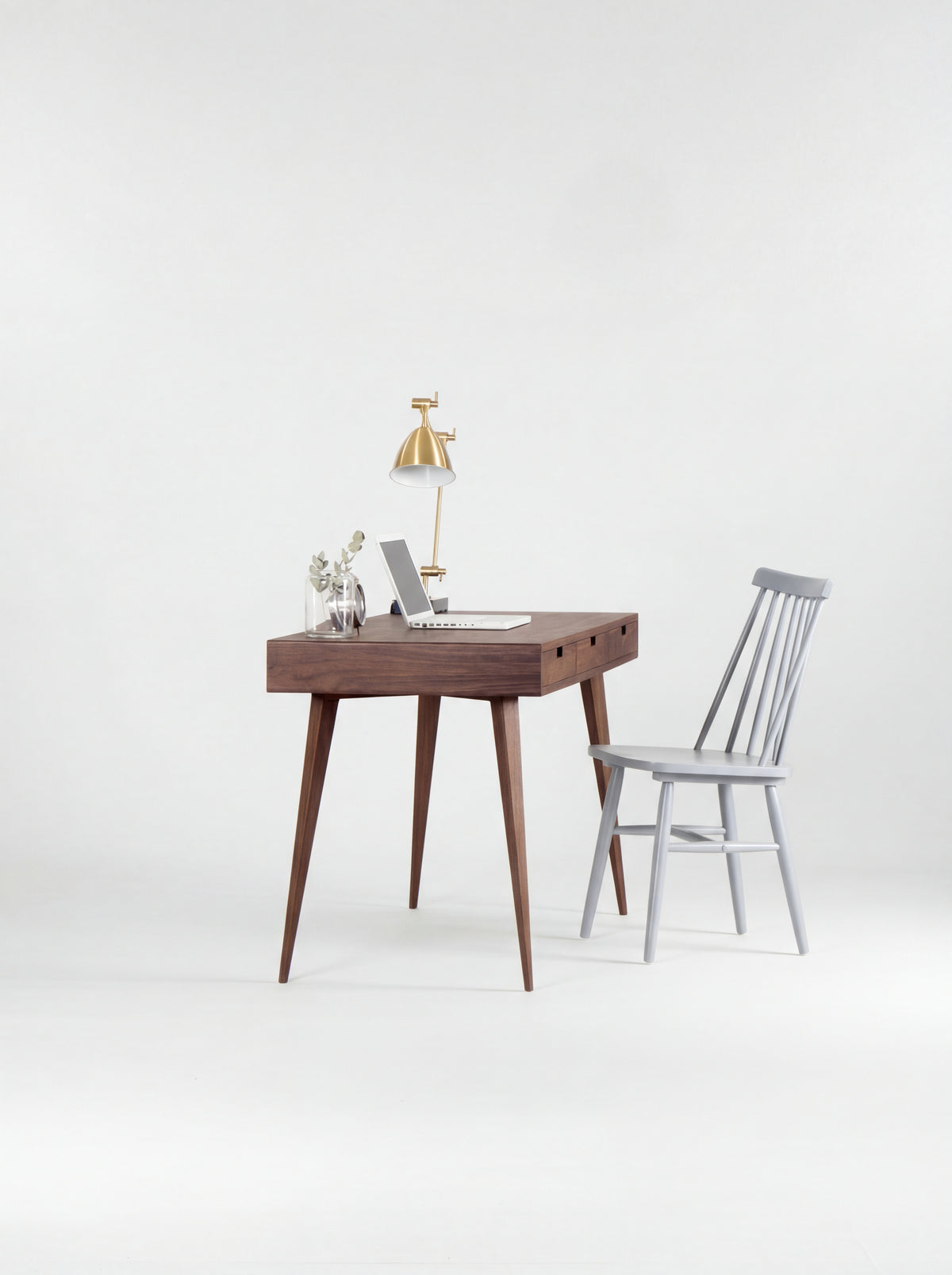 HEIM 140 desk in walnut wood seen from the short end, with splayed legs and a grey spindle chair beside it