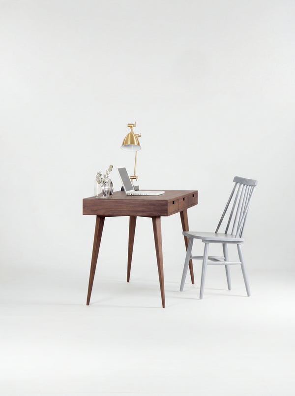 HEIM 140 desk in walnut wood seen from the short end, with splayed legs and a grey spindle chair beside it