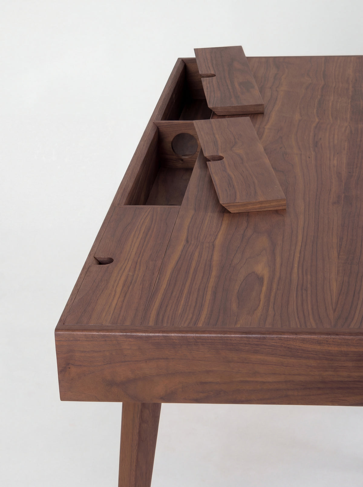 Two lifted cable flaps on the HEIM 140 desk in walnut wood reveal compartments with round cable holes