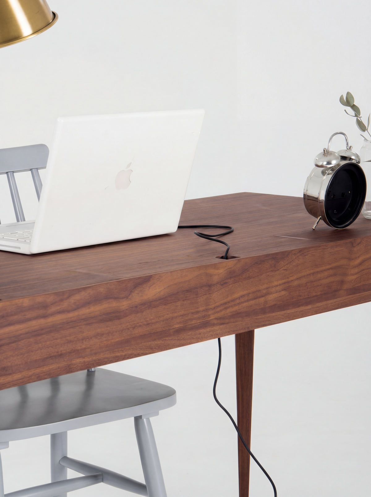 A laptop cable runs through a notch in a closed flap on the HEIM 140 desk in walnut wood